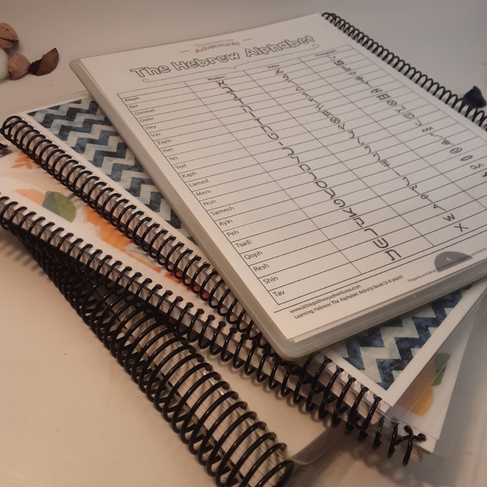 A stack of finished spiral-bound books and workbooks with black coil binding